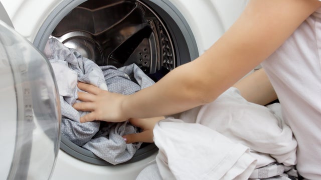 hands of a young girl put clothes in the washing machine drum